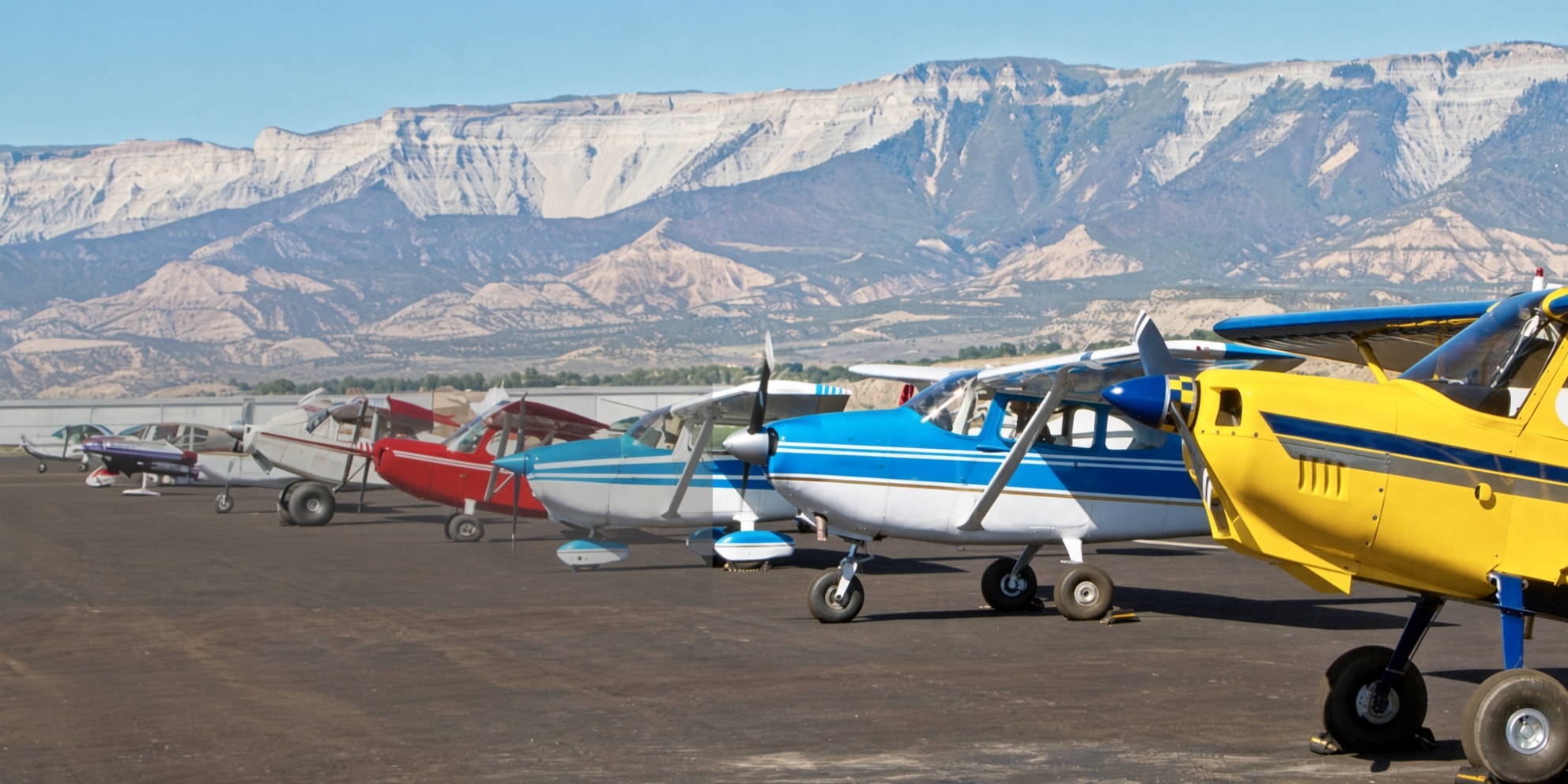 Colorful aircraft lined up at Rifle Garfield County Airport with the Colorado Rockies in the background